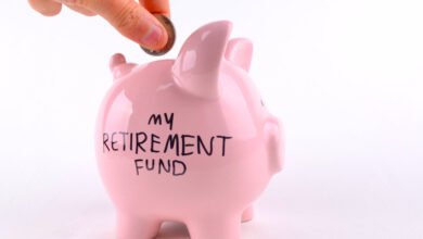 Hand putting a coin into a pink piggy bank labelled my retirement fund