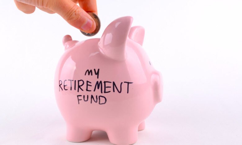 Hand putting a coin into a pink piggy bank labelled my retirement fund
